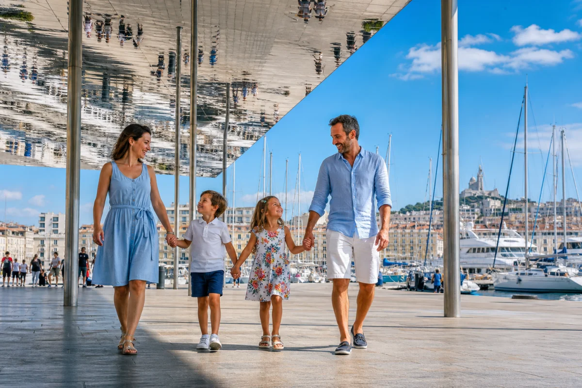 Famille souriante marchant sous l'ombrière du Vieux-Port de Marseille lors d'une sortie gratuite en famille.