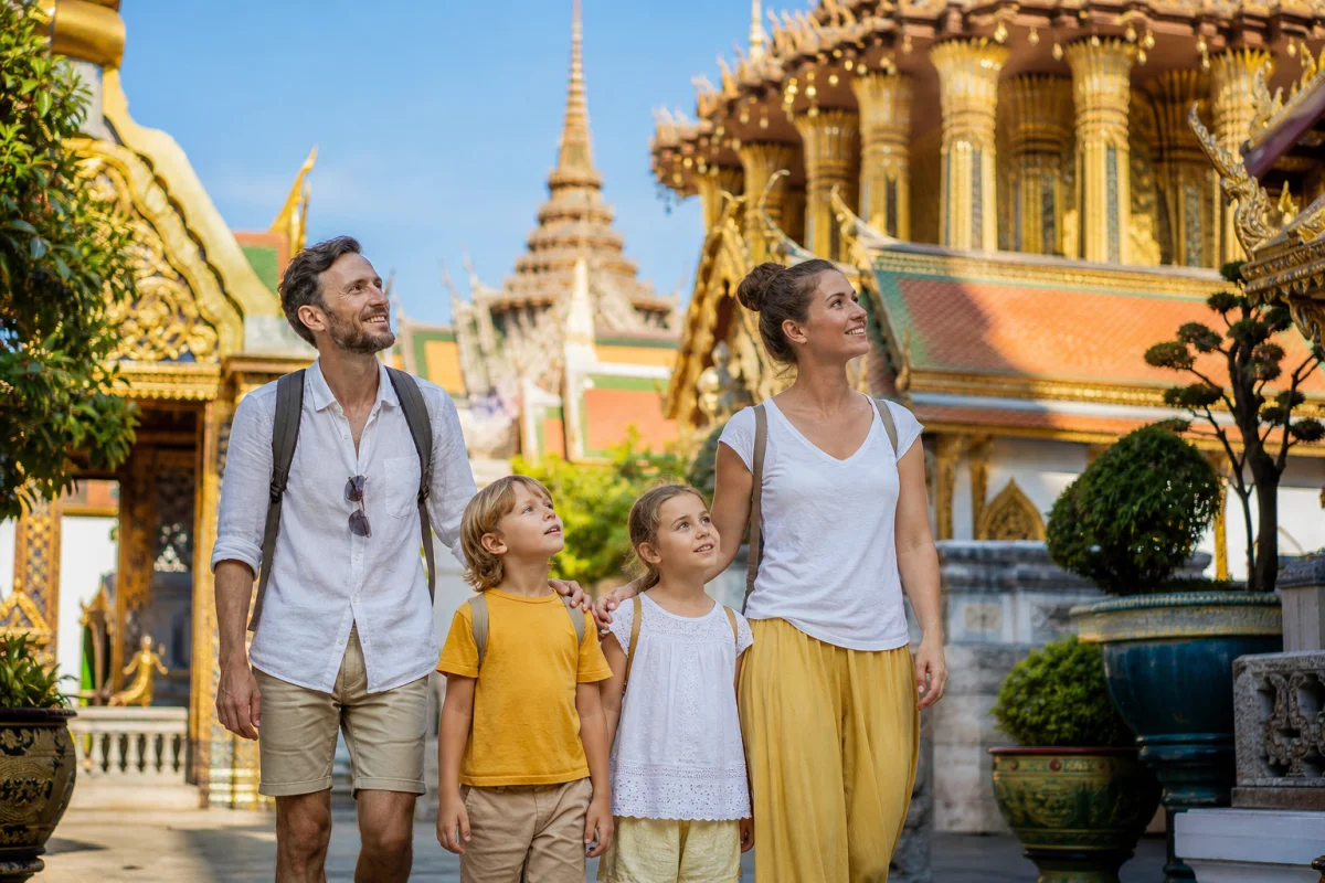 Famille souriante explorant un temple doré traditionnel lors d'un voyage en famille en Thaïlande sous un ciel bleu.